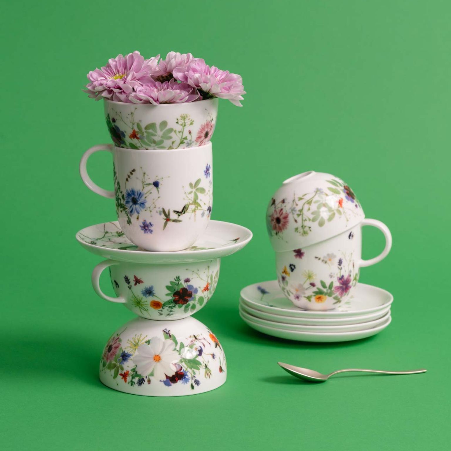 Stack of mugs, cups and small bowls from the floral Brillance Grand Air collection against a green background.